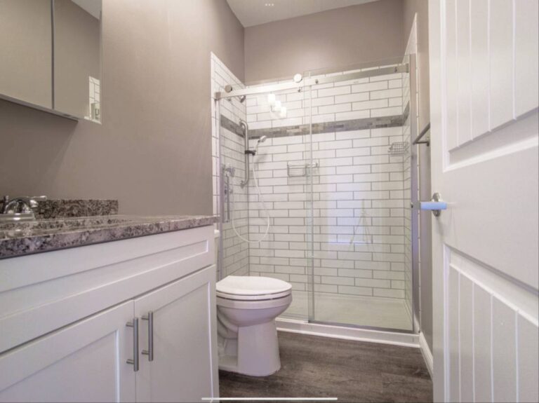 Modern bathroom with white cabinets, a granite countertop, toilet, and a glass-enclosed shower with white subway tiles.