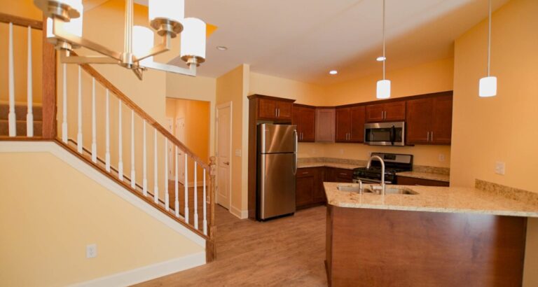 Modern kitchen with stainless steel appliances, wooden cabinets, and granite countertops next to a staircase.