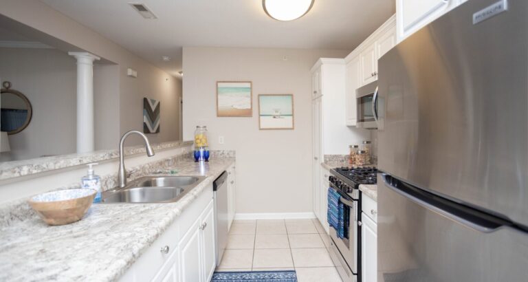 Modern kitchen with stainless steel appliances, granite countertops, white cabinets, and beach-themed wall art.