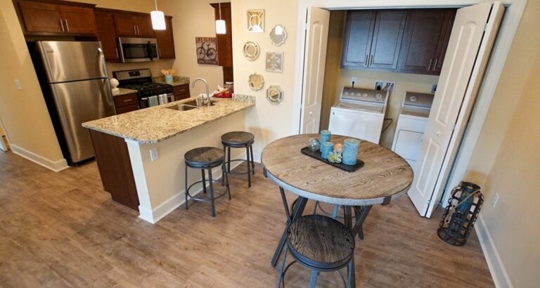 A kitchen with stainless steel appliances, a round dining table, and a laundry area with washer and dryer in the background.
