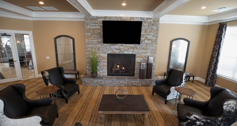 A modern living room with a stone fireplace, black chairs, a coffee table, and a TV mounted above the mantel.