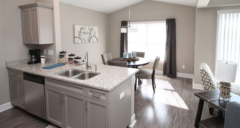 Modern kitchen with granite countertops overlooking a dining area and living room with large windows and gray decor.