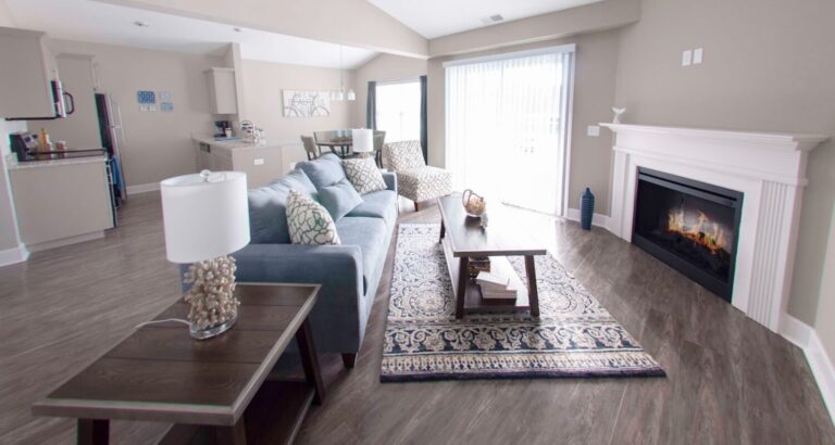 Modern open-plan living room with a fireplace, blue sofa, coffee table, and sliding glass doors to the outside.