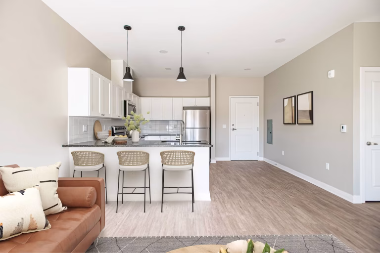 Modern kitchen with white cabinets, a breakfast bar with three chairs, and an open layout with neutral decor.