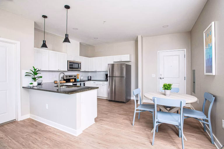 Modern kitchen with white cabinets, stainless steel appliances, and a small dining area with a round table and four chairs.