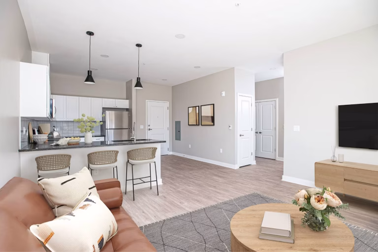 Modern open-concept living room and kitchen with neutral tones, wood floors, and minimalist decor.