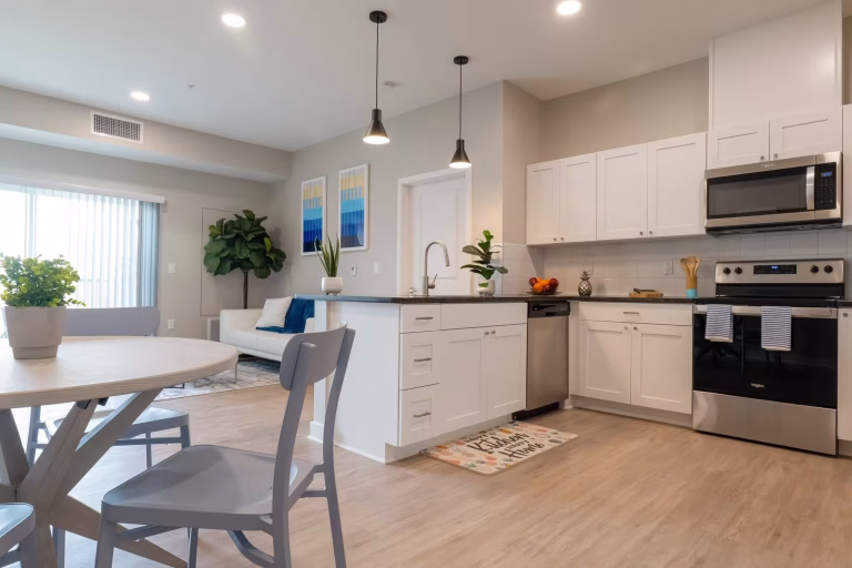 Modern open-concept kitchen and living area with white cabinets, stainless steel appliances, and neutral decor.